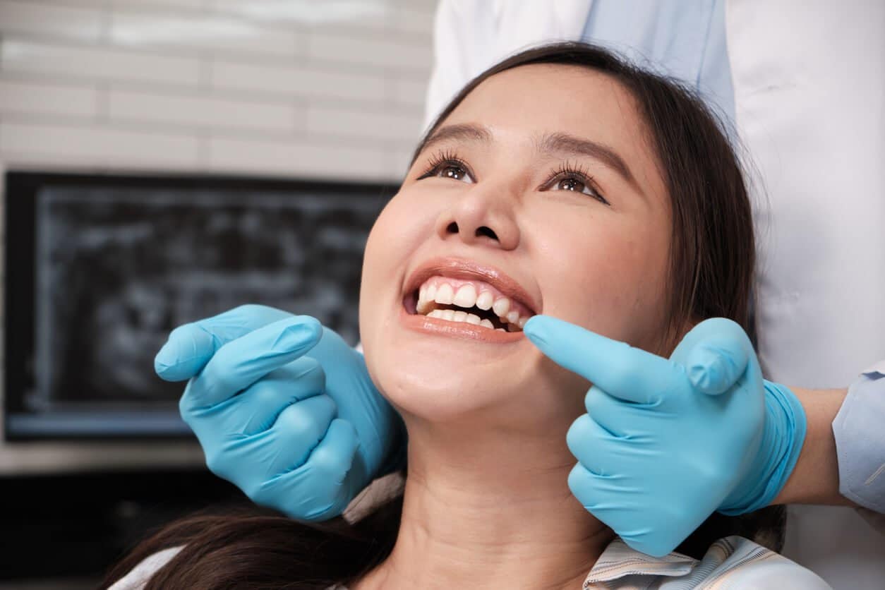How long can you keep your teeth with periodontal disease? A dentist in blue gloves examines a smiling patient’s gums during a checkup, with a dental X-ray visible in the background.